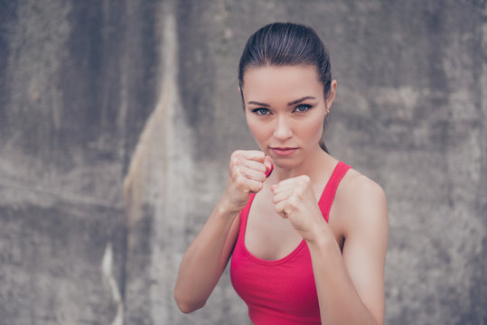Woman power, self defence concept. Close up portrait of attractive serious fit boxer, ready for fight, on concrete wall background, wearing pink fashionable sport wear