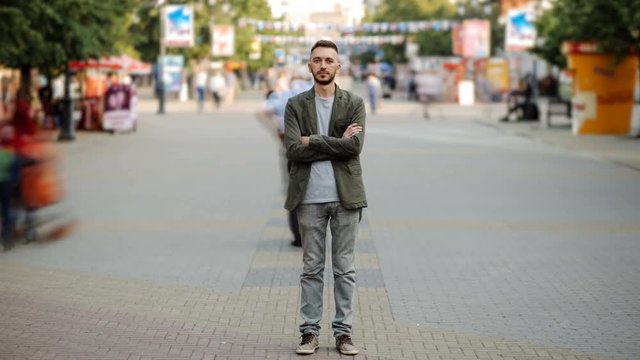 Timelapse of Young man standing still at sidewalk in crowd traffic stream with people moving fast