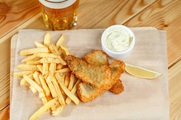 Fried fish and chips on a paper tray - Natural wooden background