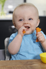 Happy Toddler Sitting At Table Eating Fresh Carrots