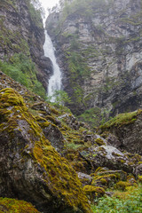 Waterfall on the mountain river in the rocky cleft with mossy overgrown stones on foreground, Norway