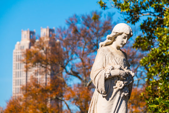The sculpture of Virgin Mary closeup on the Oakland Cemetery on the background of skyscraper in sunny autumn day, Atlanta, USA