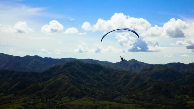 4k ultra hd. Two People ride gliding Paramotor paraglide paraplane fly in the sky with mountains midday sunny. Blue clouds.