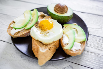 Delicious breakfast with tasty sandwiches with avocado and egg on plate on white wooden table.