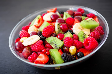 Tasty fresh fruit salad in plate on dark background. Salad with summer berries