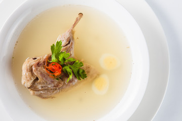 Bouillon quail egg in a white round plate on a light background (top view close)