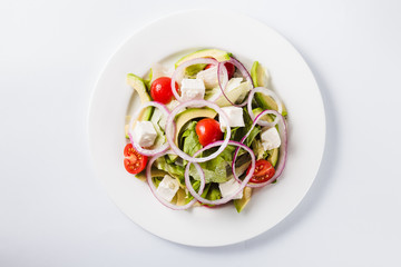 Salad with arugula and tomatoes on a round white plate on a light background (top view close)
