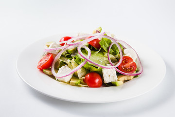 Salad with arugula and tomatoes on a round white plate on a light background (close)