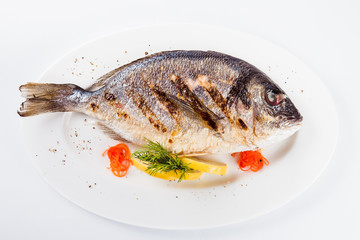 grilled dorada on a white plate on a light background (top view close)