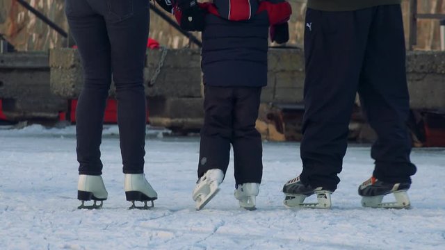 Parents teach their child to ice skate on a crowded frozen river - view at the