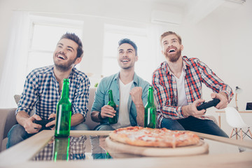 We are champions! Bachelor men`s life. Low angle of three joyful men, sitting on sofa and playing video games with beer and pizza, smiling, gesturing, enjoying  indoors at home