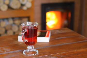 A mug of tea and a book are on a wooden table in front of the fireplace.