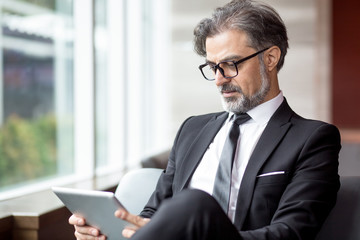 Serious senior man with tablet resting in lobby