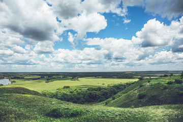 Obraz premium Beautiful natural landscape. Green hills and fields, a bright blue sky with clouds