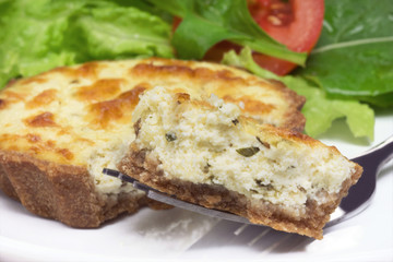 Piece of a mini wholemeal quiche in a fork close with salad in the background