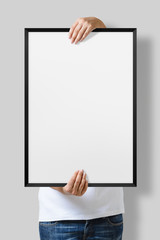 Woman holding a blank poster with black frame mockup isolated on a gray background. 