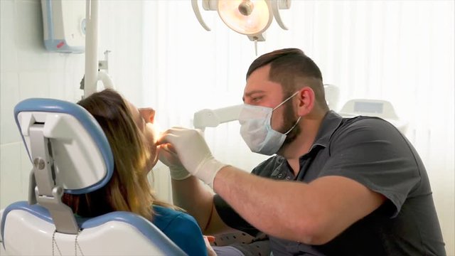 At the dental office. Man dentist using mouth mirror to examine the teeth of the young woman patient