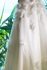 Wedding dress embroidered with crystals and pearls hangs on the white windows 