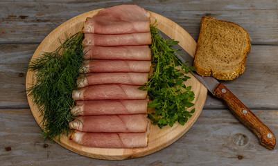 Smoked ham,basil,dill,bread and knife on a wooden plate on wooden background