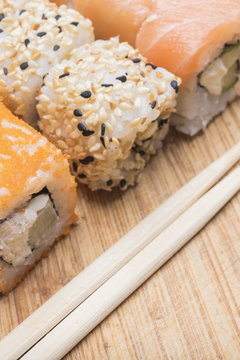 Sushi rolls with salmon, sesame, red caviar and sushi sticks lie on a light wooden board, close-up view