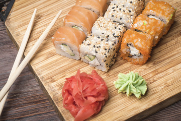 Fototapeta na wymiar Set of sushi rolls with salmon, sesame, red caviar, ginger and wasabi, sticks for sushi on a light wooden board