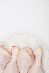 Fototapeta premium Close-up of pile of raw chicken thighs isolated on dish. Copy space. Vertical studio shot.