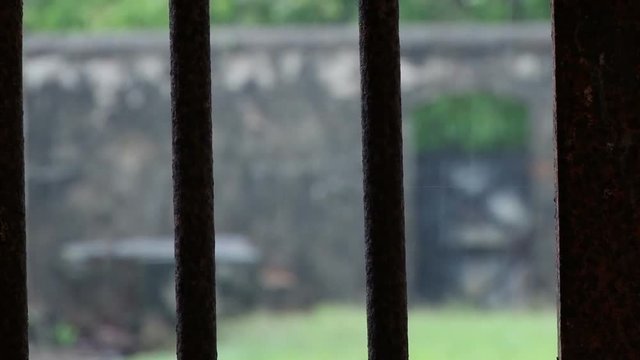 Static shot looking through jail bars to the outside on Devils Island Penal Colony in French Guiana. Heavy rain is falling