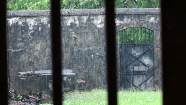 Static shot looking through jail bars to the outside on Devils Island Penal Colony in French Guiana. Heavy rain is falling