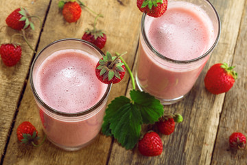 Milkshake made of fresh ripe strawberry on a rustic wooden table. Healthy fruit drink for healthy breakfast. Top view close-up shot.