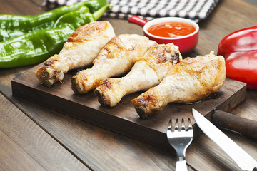 Roasted chicken thigh served on wooden board next to a vegetable and bowl with sauce. Barbecue.