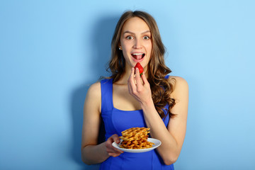 Beautiful woman eating belgian waffeles with strawberries on blue background