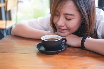Top view image of Asian woman sit with chin resting on her hands and closing her eyes smelling hot coffee on wooden table with feeling good in cafe