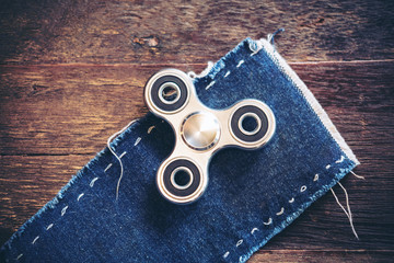 Top view image of a metal silver color fidget spinner on jean cloth with wooden table background