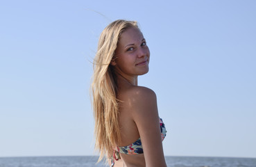 Fototapeta na wymiar Blond girl in a bikini on the beach. Beautiful young woman in a colorful bikini on sea background