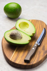 Freshly sliced ripe green avocado and knife on wooden board.