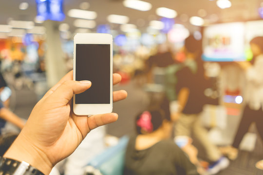 Close Up on smart phone in a man hand and blurred image of a people in the airport background.