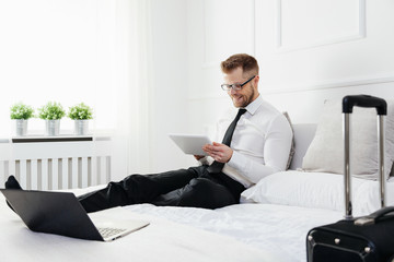Businessman on bed working with a tablet and laptop from his hotel room