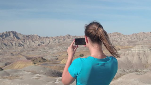 CLOSE UP: Cheerful young woman traveler taking photos of stunning Badlands National Park on a sunny day in South Dakota, USA. Happy girl exploring desert wilderness and photographing with smart phone
