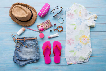 Summer concept with women's casual summer clothes with accessories items on blue rustic wooden board background