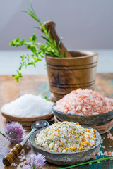 Three different types of natural salt in stone bowls on wooden surface. White sea salt, pink Himalayan salt, Spiced salt with rosemary