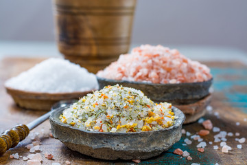 Three different types of natural salt in stone bowls on wooden surface. White sea salt, pink...