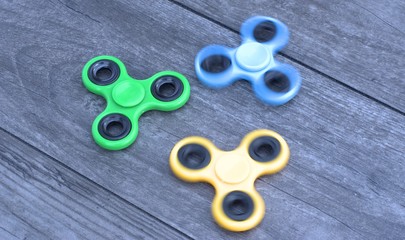 Three fidget hand spinner stress relieving toy on a wooden background.