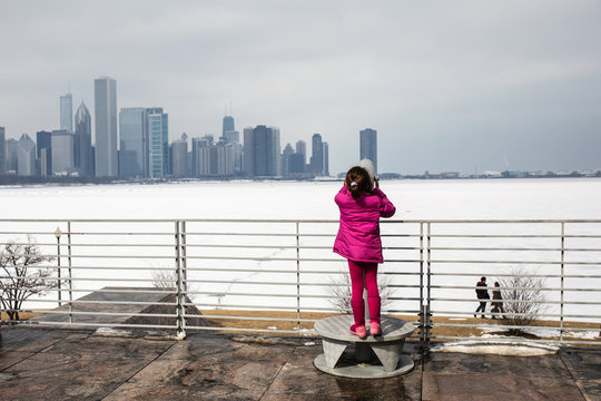 Young girl using coin operated binoculars, looking across frozen Lake Michigan, at Chicago city, USA