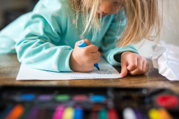 Young girl at home, drawing on white paper, art kit in front of her, mid section