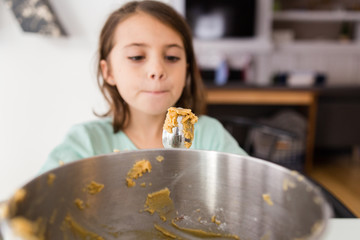 Young girl eating cookie mix from spoon