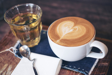 Closeup image of a cup of hot coffee and a tea glass on vintage wooden table in cafe
