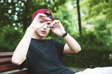 A long-haired hipster in a cap sits on a bench and spins a fidget-spinner