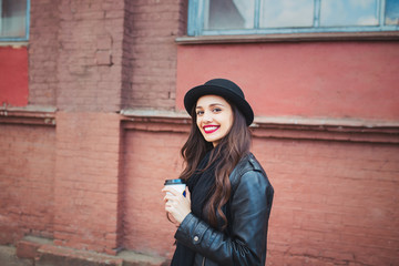 Young stylish woman in a city street drinking coffee and having fun
