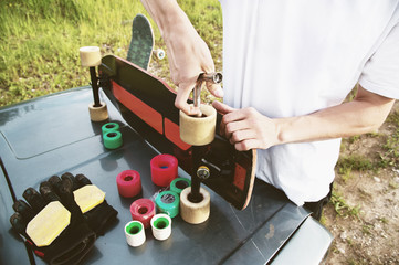 A close-up of a young guy changes his wheels on his longboard and adjusts the suspension.