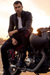 Handsome rider guy with beard and mustache in black leather biker jacket sit on classic style cafe...